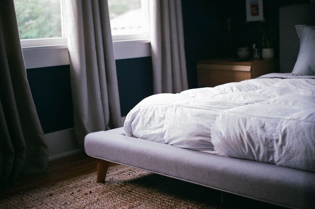 cama con cobertor blanco al lado de ventana con cortinas grises
